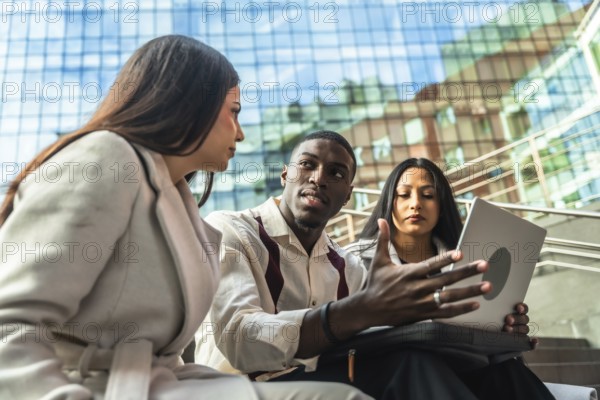 Diverse business team meets outdoors in an urban setting, sharing ideas over a laptop while
