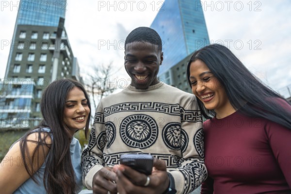 Diverse friends laughing and smiling while gathered on a city street, looking at a smartphone and