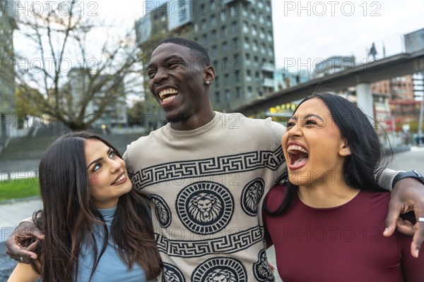 Three multiethnic friends laughing and embracing on a city street, sharing joyful, candid moments