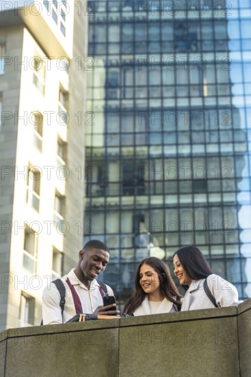 Three diverse students, a man and two women, smiling and looking at a smartphone, sharing content