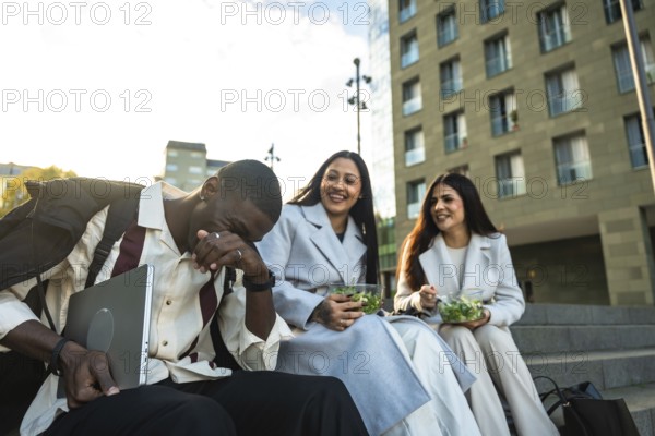 Diverse colleagues enjoying their lunch break outdoors, sitting on stairs in the city, laughing and