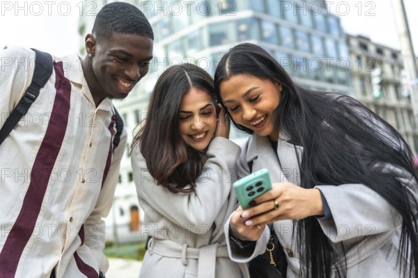 Diverse group of young adult friends smiling and laughing while watching something on a smartphone