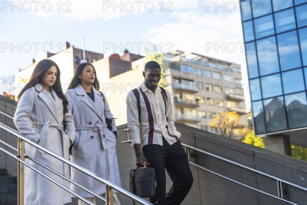 Three diverse business colleagues descending outdoor stairs, walking together after work or during