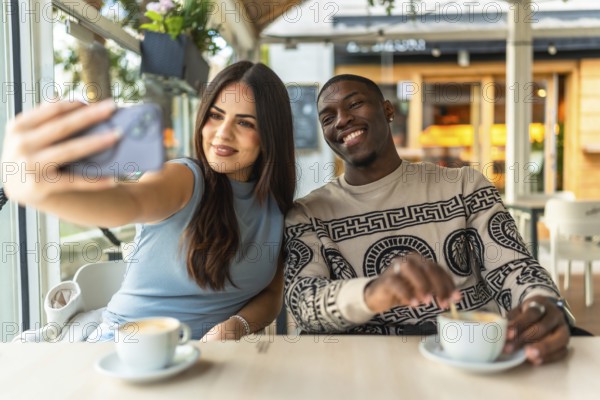 Happy diverse couple smiling while taking a selfie with a smartphone at a coffee shop, enjoying