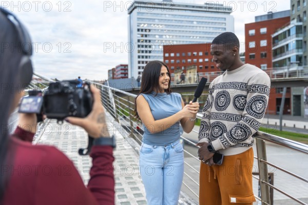 Journalist holding a microphone and interviewing a smiling young man on a modern urban bridge while