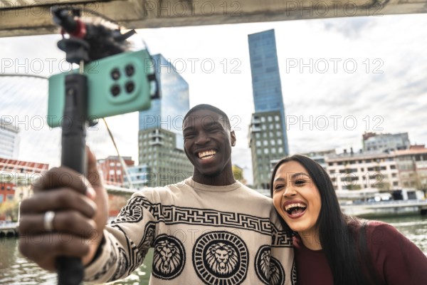 Diverse young couple vlogging together outdoors in a modern city, smiling and laughing as they live