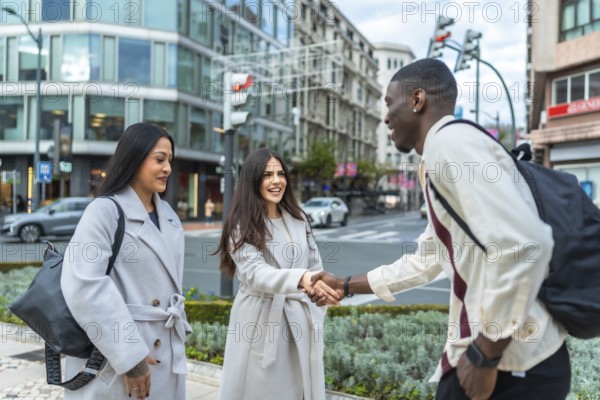 Diverse young adults meeting on a city sidewalk, one woman shaking hands with a man, while another