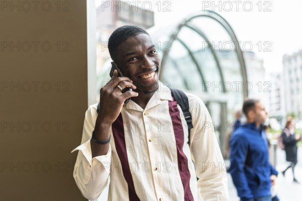 Smiling young black man talking on his mobile phone in an urban setting, enjoying a conversation
