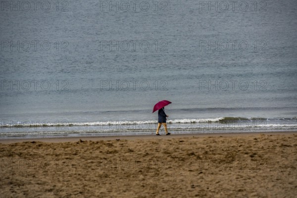 Person with red umbrella walking along the beach, calm sea in the background, winter break, on