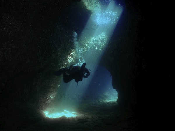 A diver floats through a mystical underwater cave, flooded with blue light. Fraskeric dive site,
