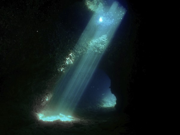 Sun rays illuminate the interior of a dark underwater cave with blue light reflections. Fraskeric