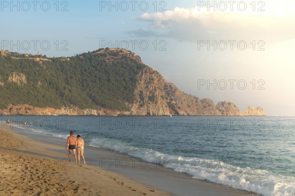 A couple walk along an empty Cleopatra Beach at sunset in the Turkish holiday resort town of Alanya