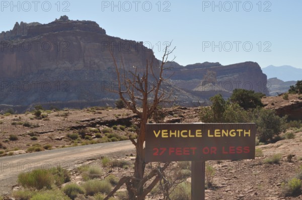 Desert landscape with vehicle length road sign and rocky mountain range in the background, Capitol