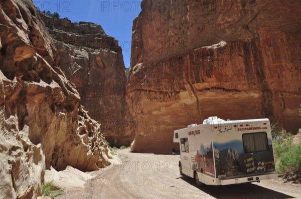 Motorhome traveling in a canyon with massive red rock structures under clear skies, Capitol Reef