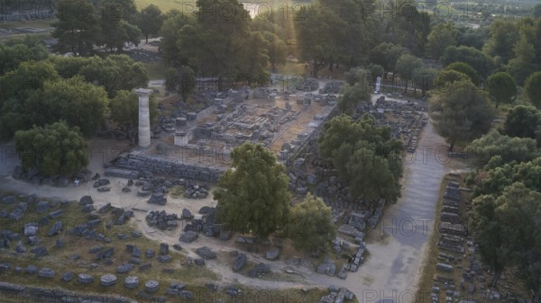 Temple of Zeus in backlight, ancient ruins surrounded by trees, with a single stone pillar amidst