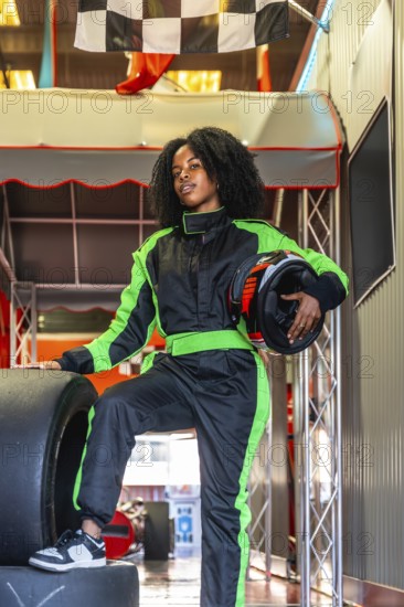 Young black woman standing confidently in a green and black race suit, holding a helmet and resting
