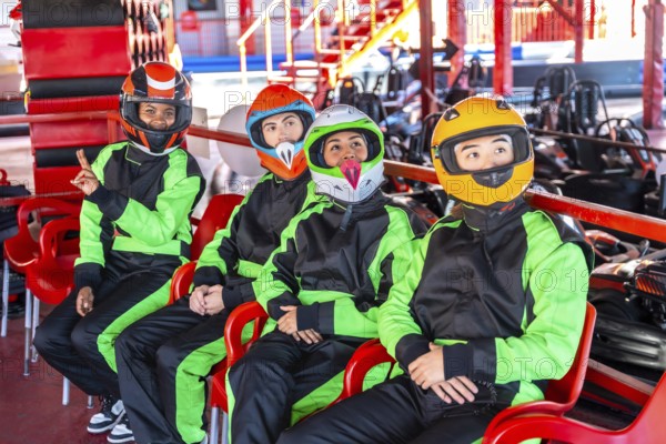 Group of young diverse adults wearing race suits and helmets, sitting on chairs and anticipating a