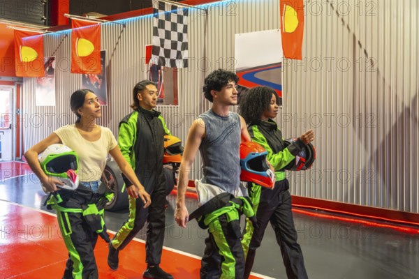 Group of diverse gen z friends holding racing helmets and walking in an indoor karting facility,