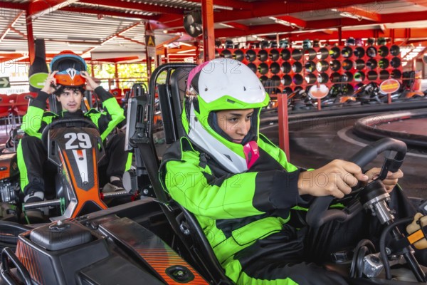 Two young men, one putting on his helmet and another holding a steering wheel, are preparing for a