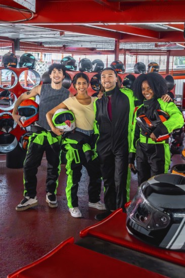 Group of diverse friends smiling and holding racing helmets, wearing go kart suits, and standing on