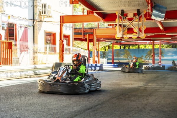 People wearing helmets and green racing suits driving go karts around an outdoor track, enjoying