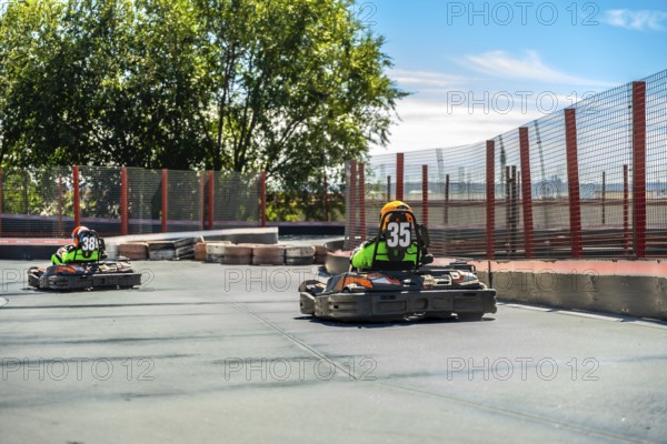 Two competitive go karts with drivers wearing helmets and number vests driving quickly on an