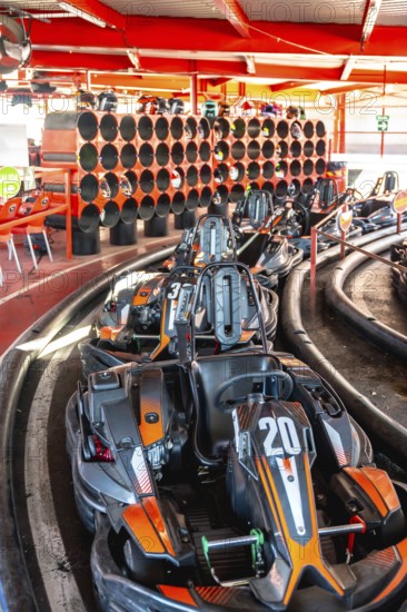 Go karts with orange and black details resting in a queue at the starting line of an indoor track,