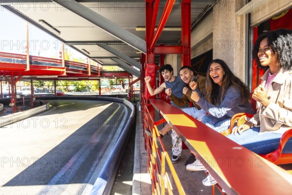 Diverse group of young friends is enthusiastically cheering and watching a go kart race from an
