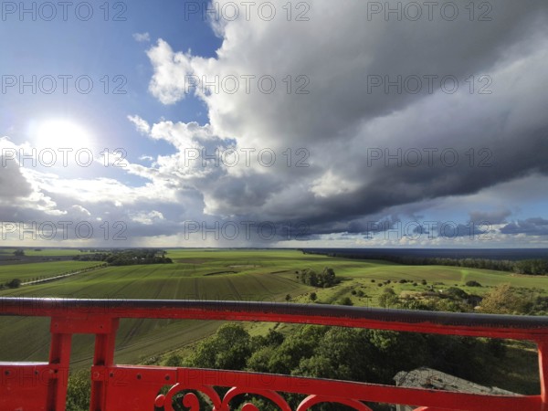 View of green fields under dramatic sky with dark clouds, red railings in the foreground and