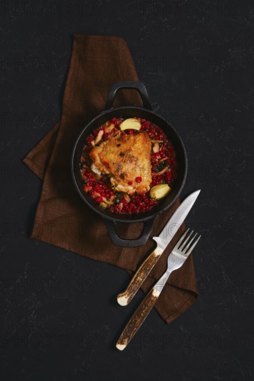 A chicken dish is served in a black cast iron pot. The pot contains spicy lingonberry sauce. Two