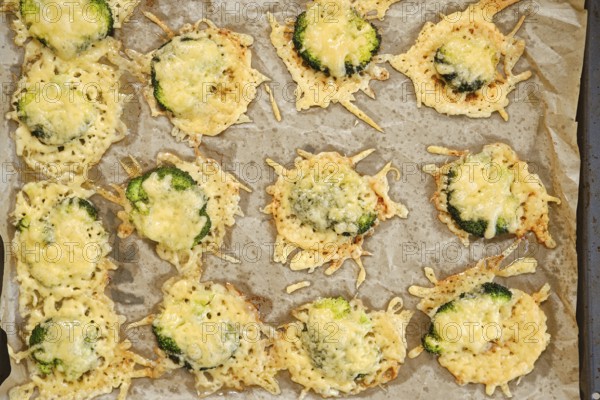 Broccoli pieces are smashed and spread on a baking sheet. They are topped with cheese and placed in