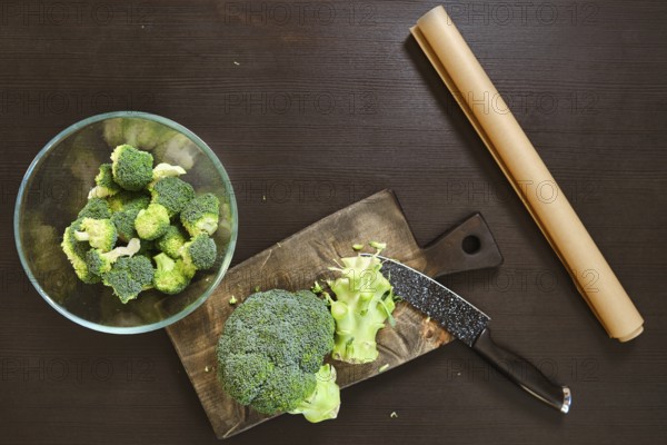 Broccoli is being cut on a wooden board. A bowl of chopped broccoli sits nearby. The kitchen is