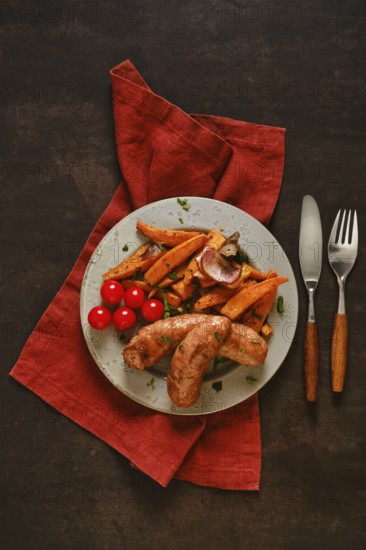 Natural casing sausages are placed on a green plate alongside roasted sweet potatoes and cherry