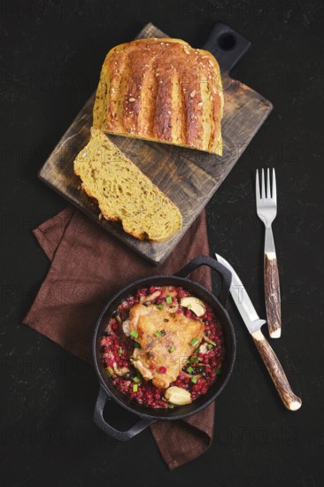 Top view of roasted chicken thigh with lingonberry in a pan on a brown cloth. Freshly baked bread