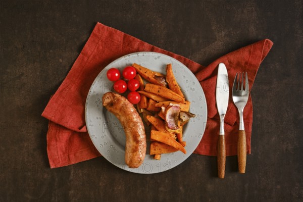 A plate holds natural casing sausages alongside roasted sweet potatoes and cherry tomatoes. The