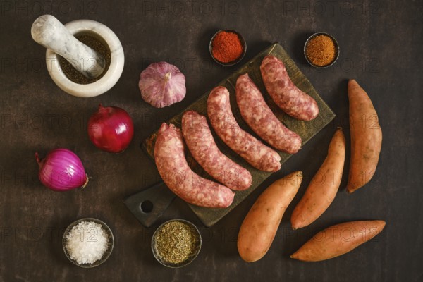 Natural casing sausages on a wooden board alongside sweet potatoes, garlic, onions, and various