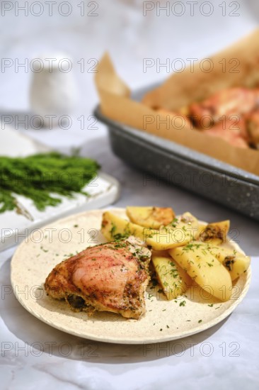 Roasted chicken and potato wedges. Baking tray is seen in the background with more chicken. The