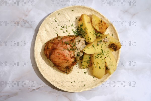 A chicken thigh is placed beside several pieces of seasoned potatoes on a round plate. The dish has