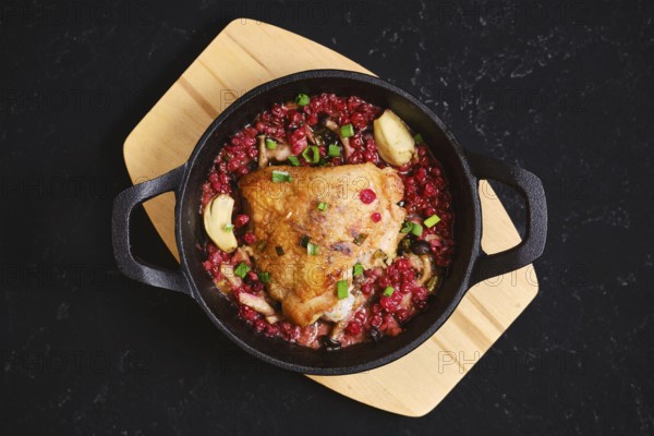 Top view of chicken thigh roasted with lingonberry and garlic. The skillet is placed on a wooden