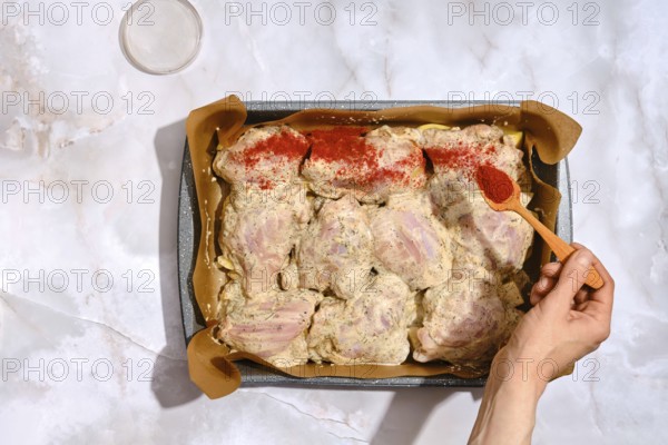 A person spreads smoked paprika over chicken thighs placed in a baking tray lined with parchment