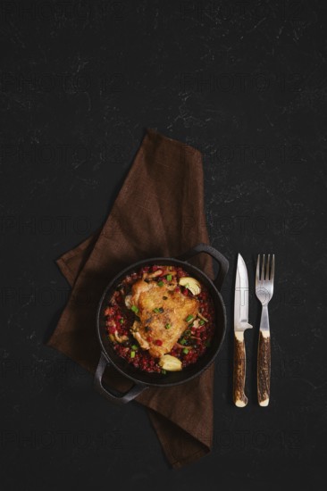 A warm bowl holds a tasty meal featuring chicken with lingonberry placed on a brown cloth. A knife
