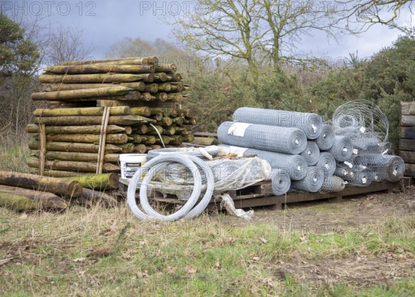 Agricultural fencing supplies wooden fence posts, rolls of wire stacked outdoors post-and-wire