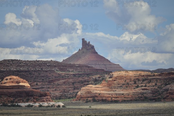 Distinctive pointed rock rises high, surrounded by red rocks and dramatic cloud formations,