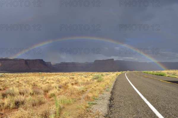 Another rainbow over a long, empty road in a colorful desert landscape with cloudy sky, Canyonlands
