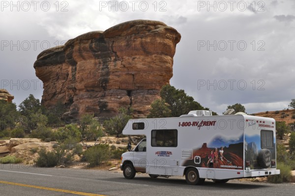 Motorhome standing on a road in front of a distinctive rock formation under a cloudy sky,