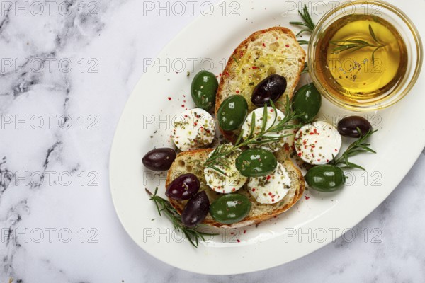 A plate with a snack, ciabatta bread with cheese and olives, olive oil, spices and herbs, top view,