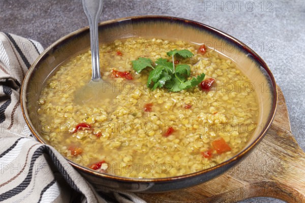 A hearty lentil soup is presented in a rustic bowl, featuring vibrant tomato pieces and fresh