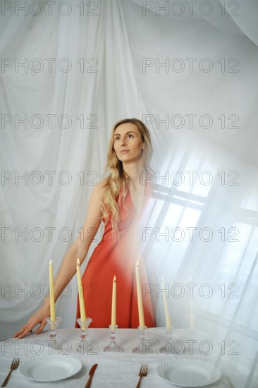 A woman stands near a table that has candles, plates, and cutlery. The soft light comes through the