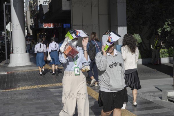 Bangkok, Thailand. March 25th 2025. People shield their faces from the bright sun and wear face