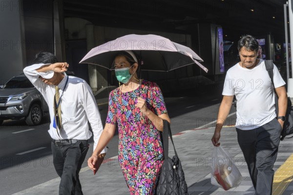 Bangkok, Thailand. March 25th 2025. People shield their faces from the bright sun and wear face